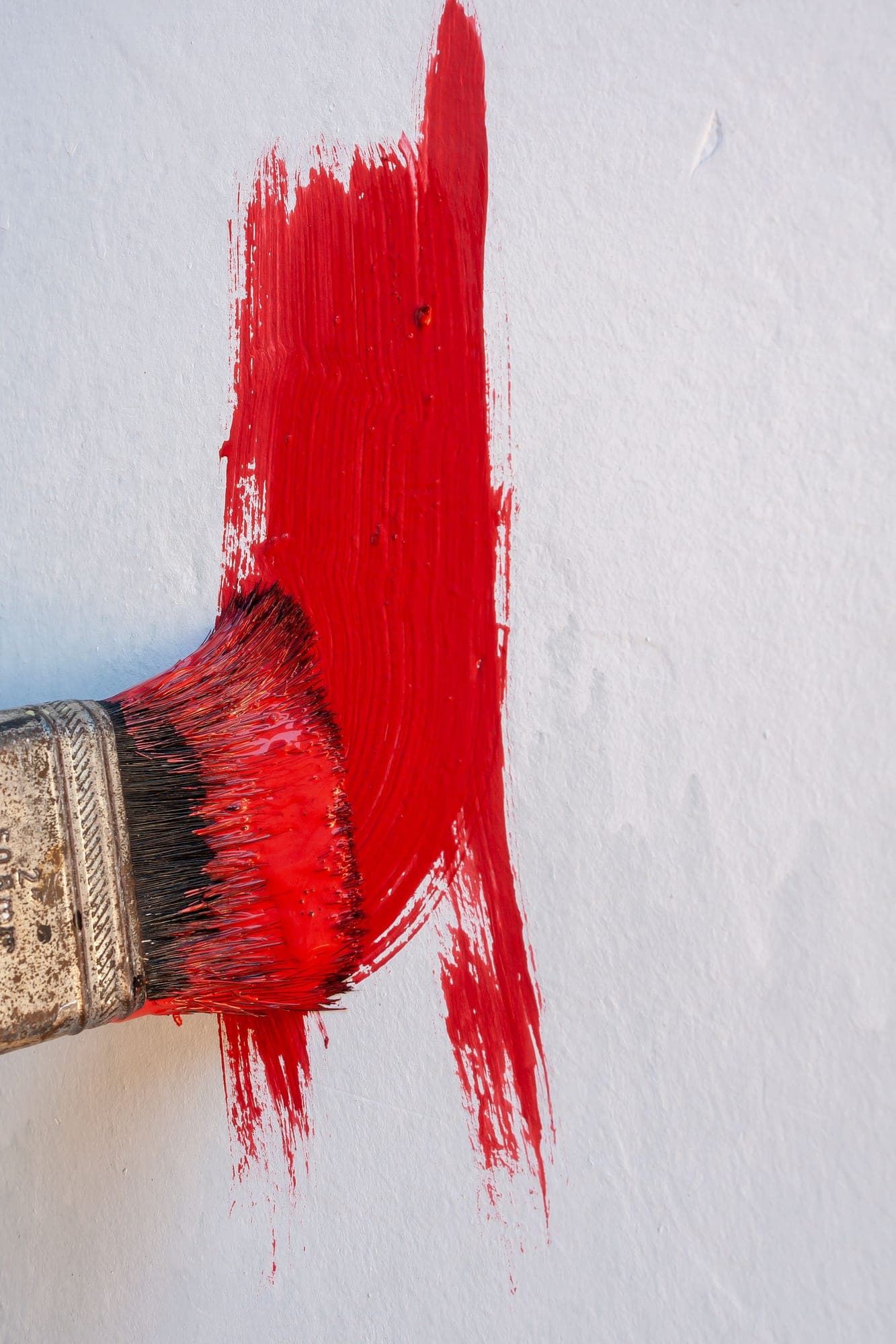 A broad, decisive stroke of vivid red paint drawn across a white wall with a loaded brush
