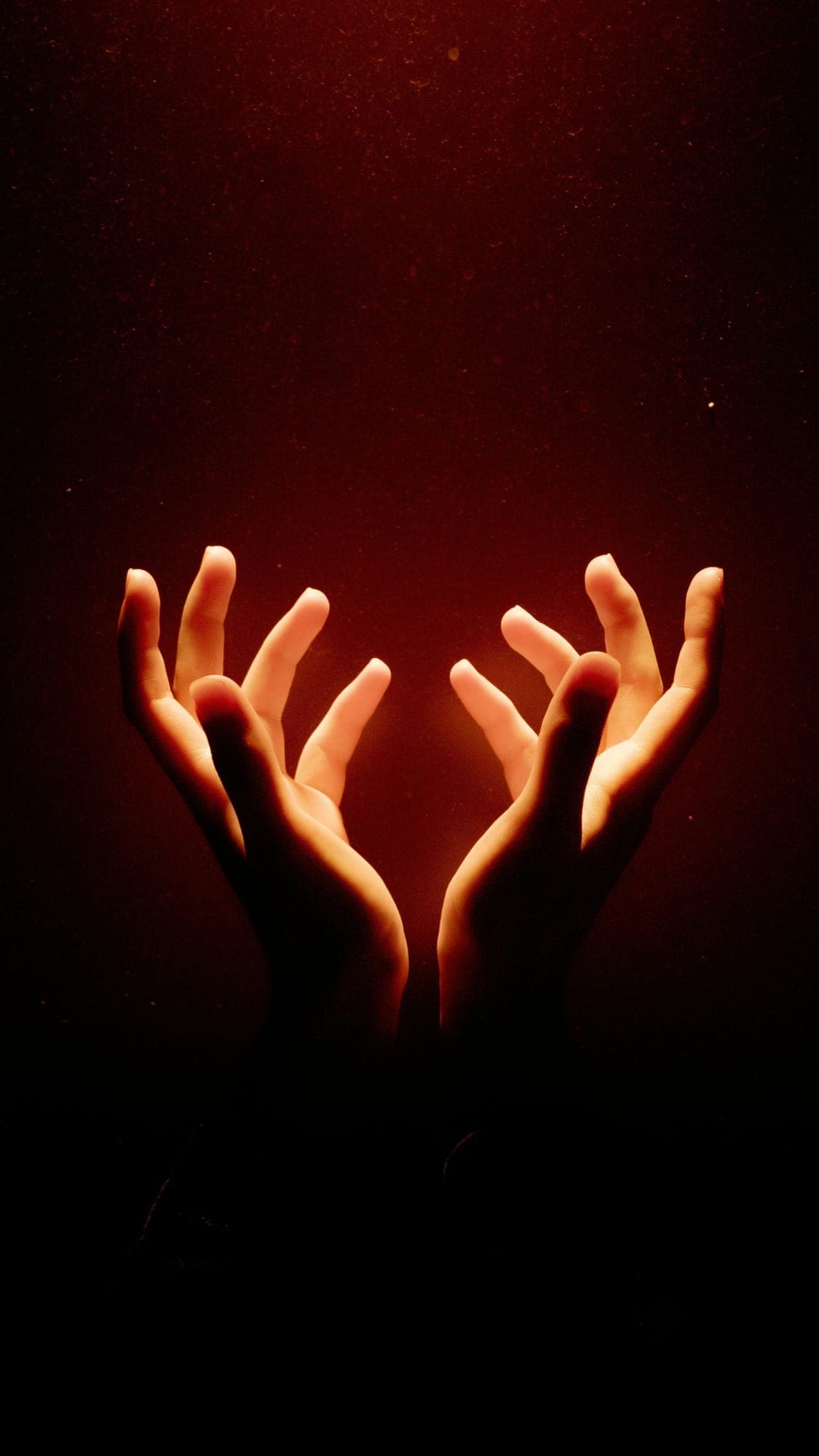 Two open hands lifted out of deep shadow toward a single warm glow of light