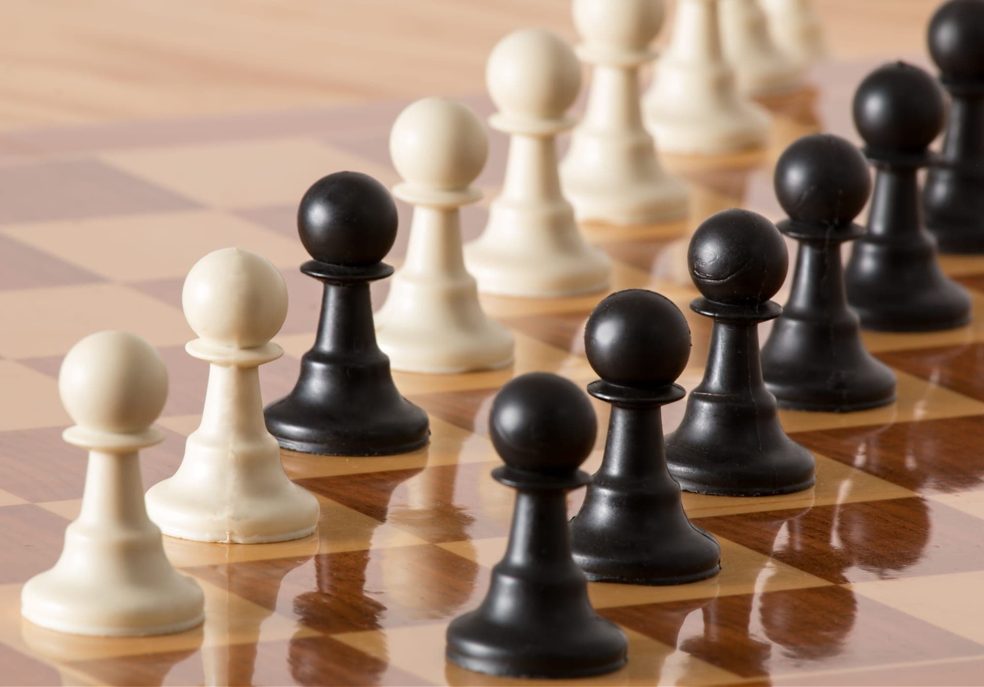 Rows of black and white chess pawns facing one another across a polished wooden board