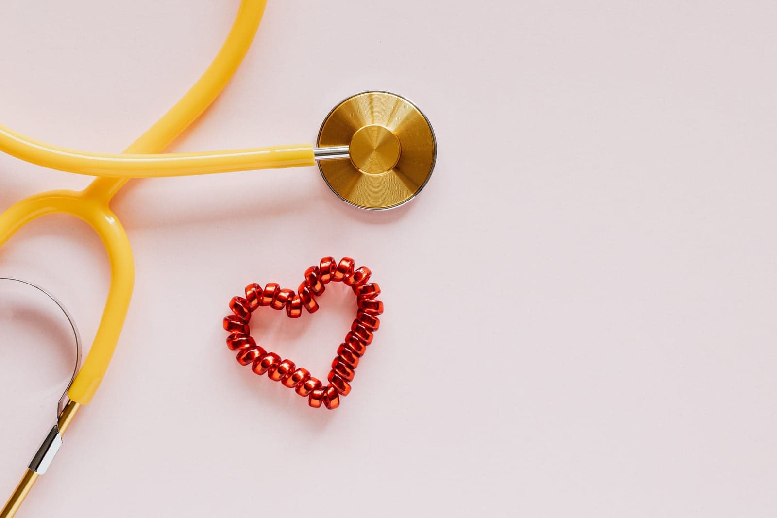 A yellow stethoscope beside a small red heart shape on a soft pink background