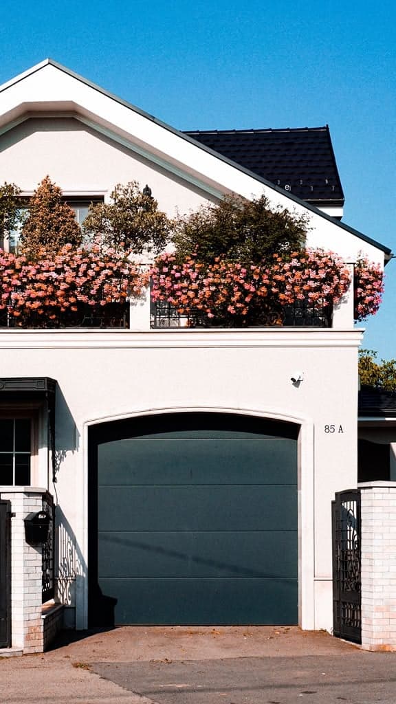 A home's balcony overflowing with pink flowering plants above the garage