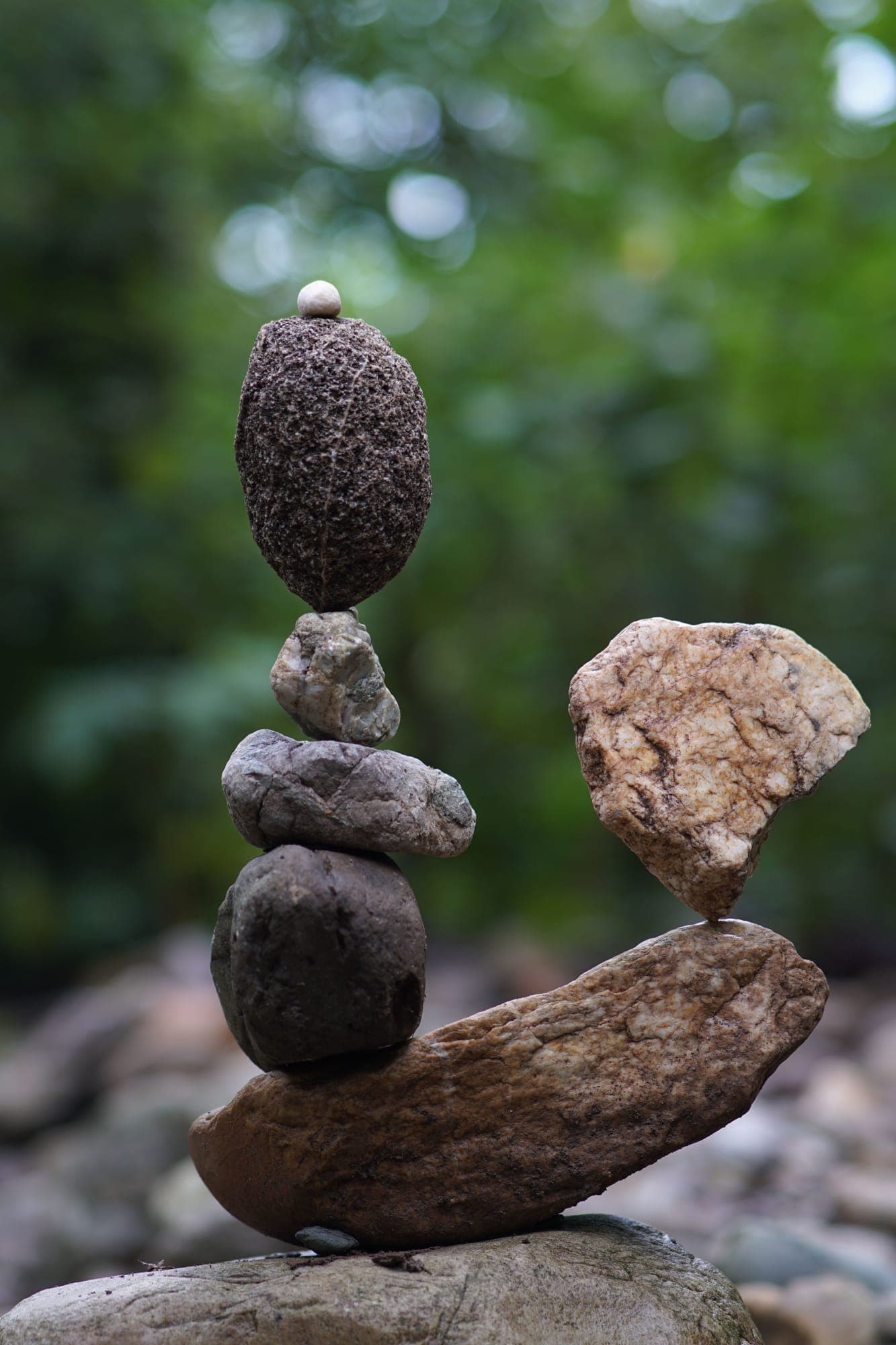 A carefully balanced stack of river stones holding steady against a green, wooded background